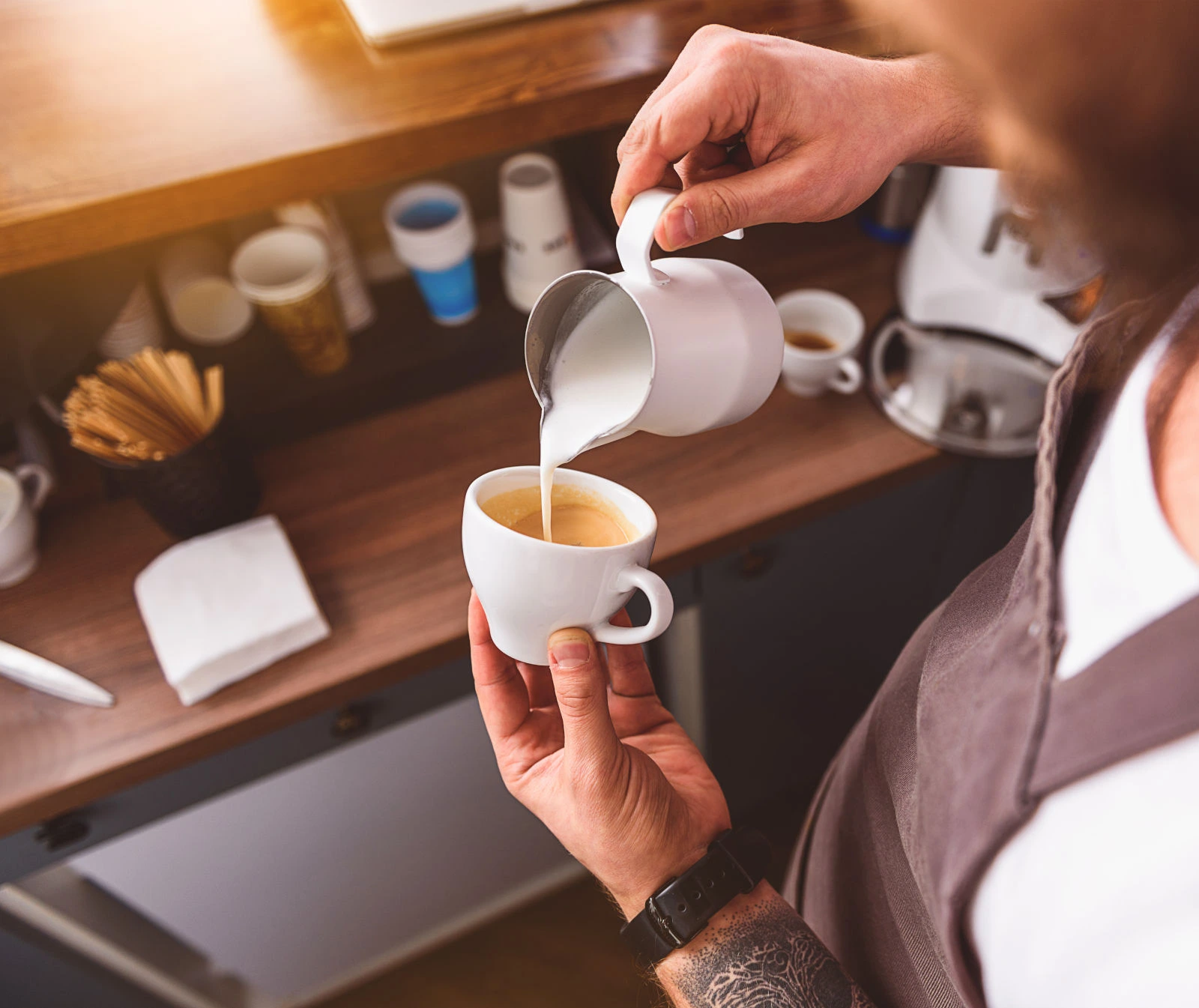 Un barista vierte bebida vegetal en una taza de café espresso, capturando un momento de preparación en una cafetería.